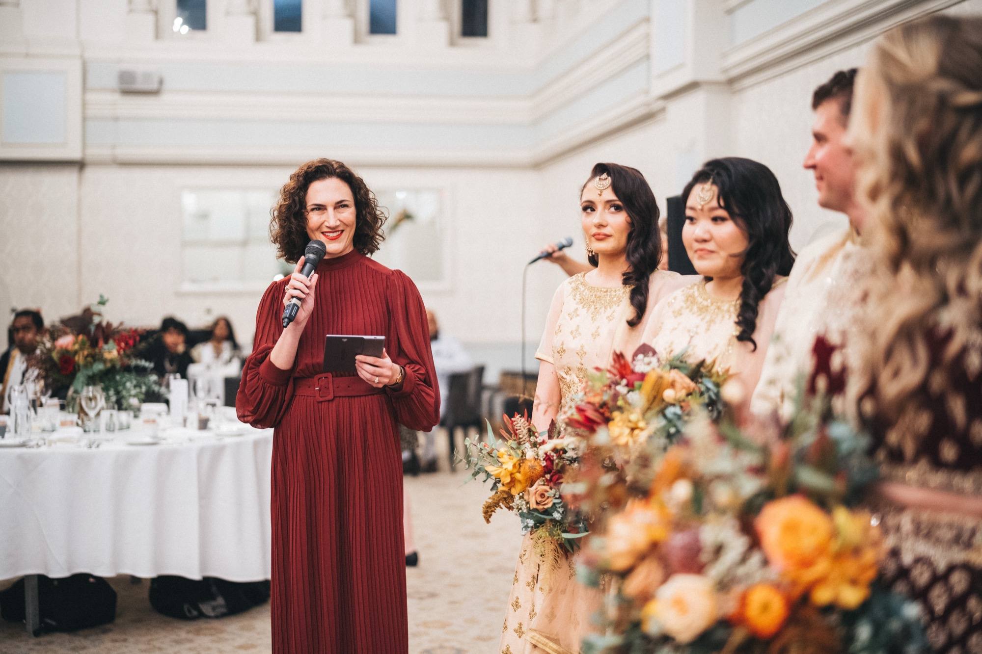 Marriage celebrant Melissa Soncini speaking into a microphone at an indoor wedding reception