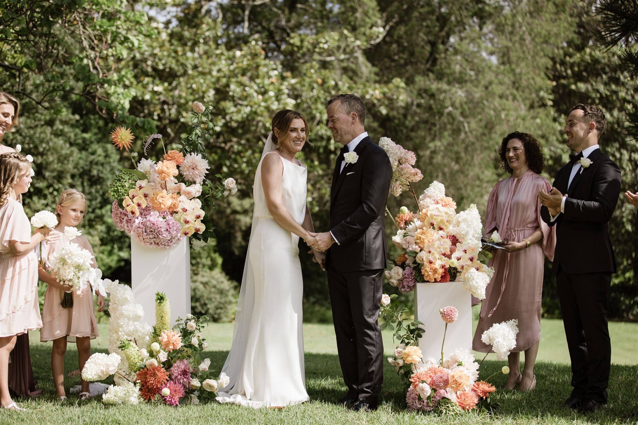 A couple holding hands during their garden wedding ceremony, surrounded by colourful floral arrangements